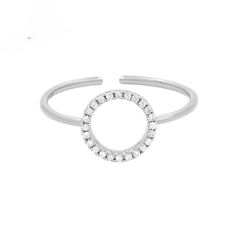 A silver-toned open cuff ring featuring a central circular motif paved with small clear stones, shown on a plain white background.