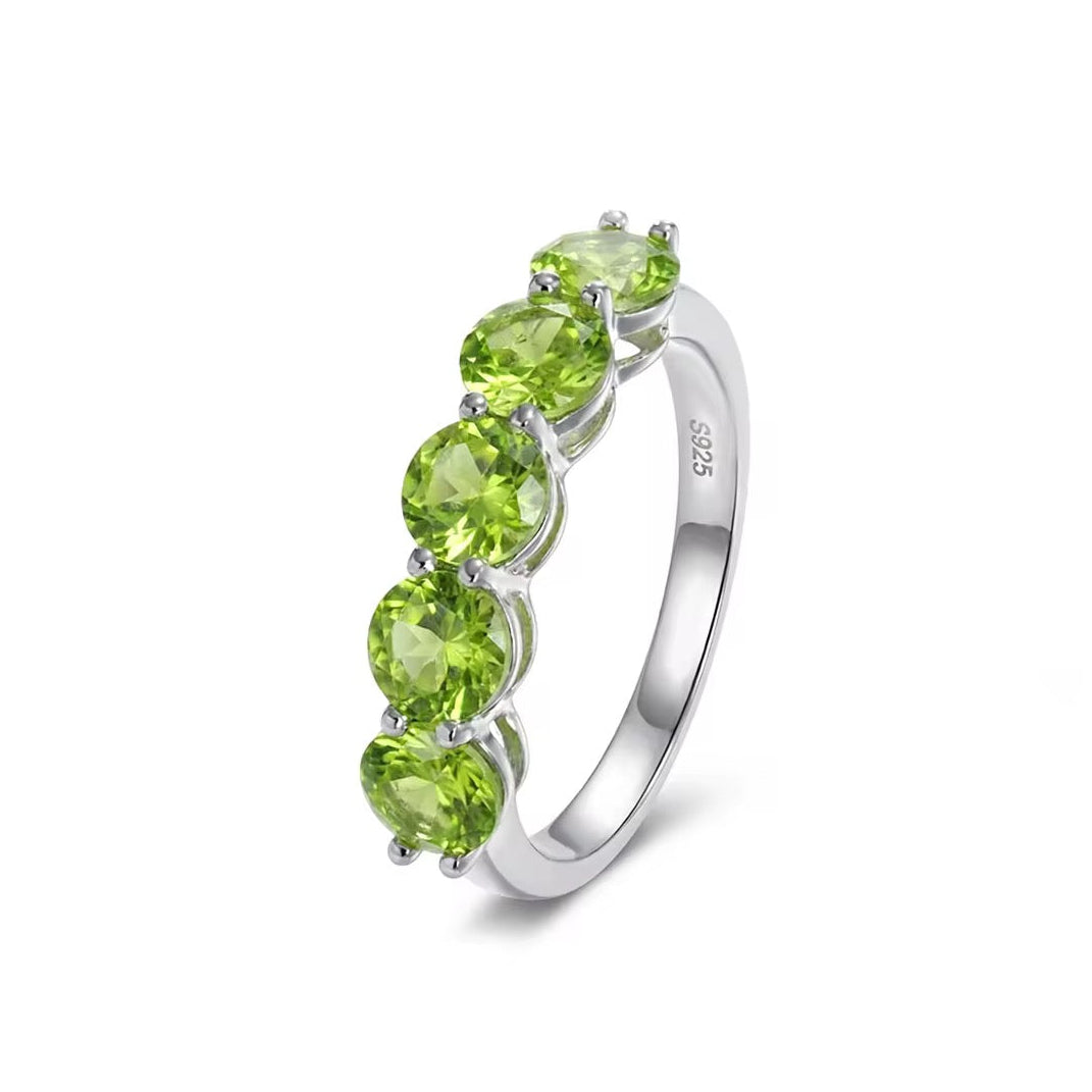 A sterling silver ring featuring five round-cut green peridot gemstones in a row, set against a clean white background.