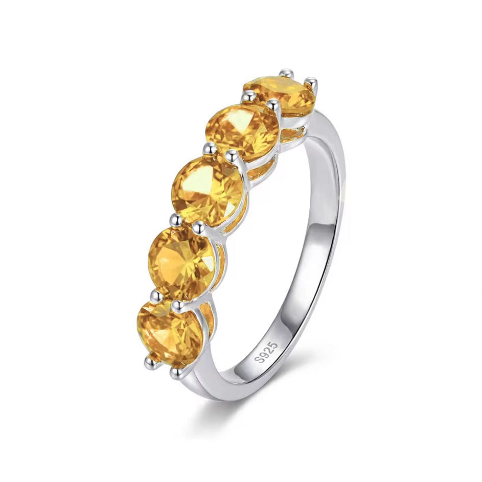 A silver-toned eternity ring featuring five round-cut yellow citrine gemstones set in a row, shown on a clean white background.