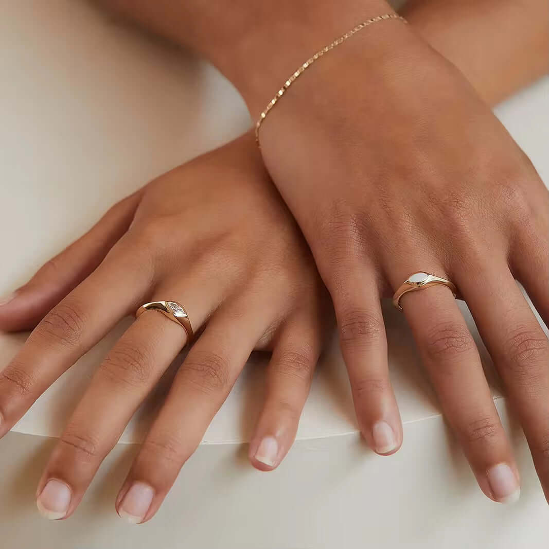 Two hands adorned with sterling silver rings featuring synthetic opals, showcasing elegance and style with a gold-plated bracelet.