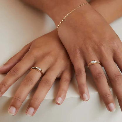 Two hands adorned with sterling silver rings featuring synthetic opals, showcasing elegance and style with a gold-plated bracelet.