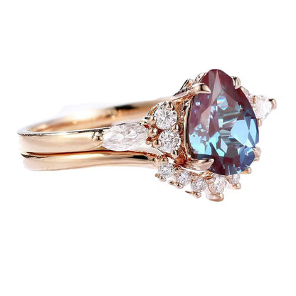 A rose gold ring with a pear-cut Alexandrite center stone and surrounding clear accent stones, shown on a plain white background.