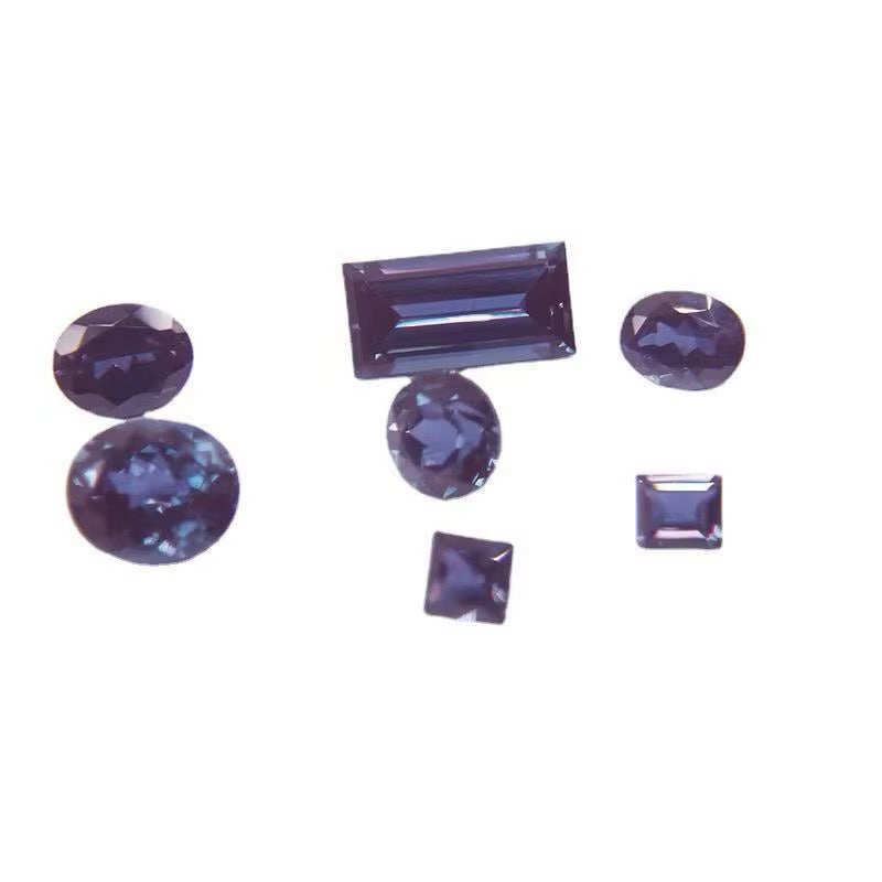Six dark blue to purple faceted Alexandrite gemstones in different cuts, including oval, round, rectangular, and square shapes, arranged on a plain white background.
