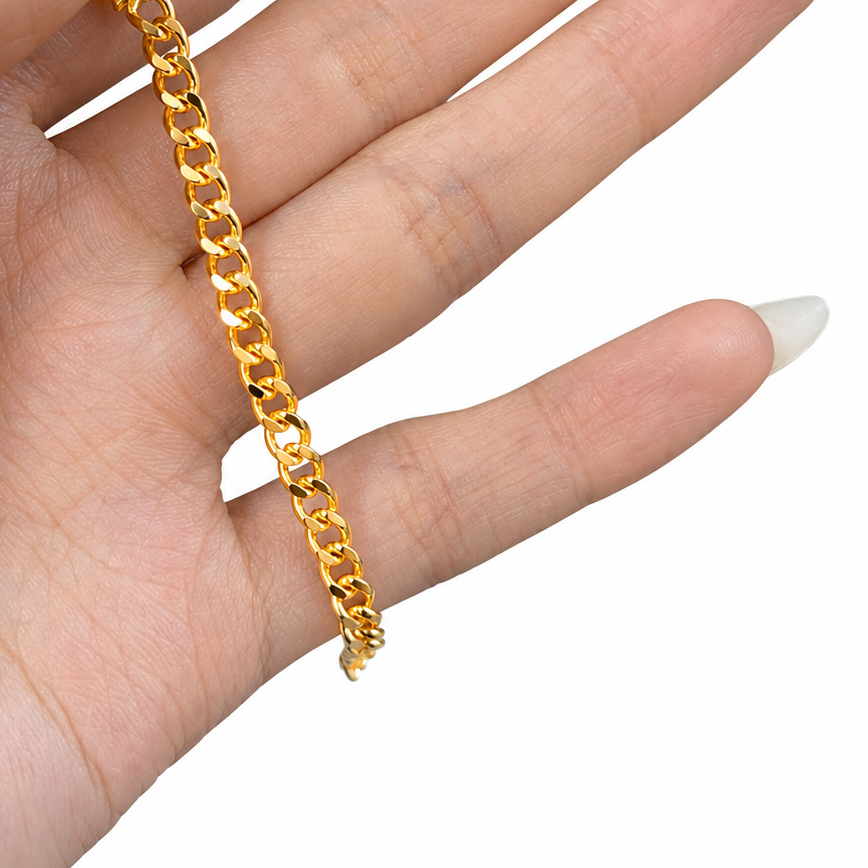 A close-up of a hand holding a shiny gold Cuban link chain against a plain white background.
