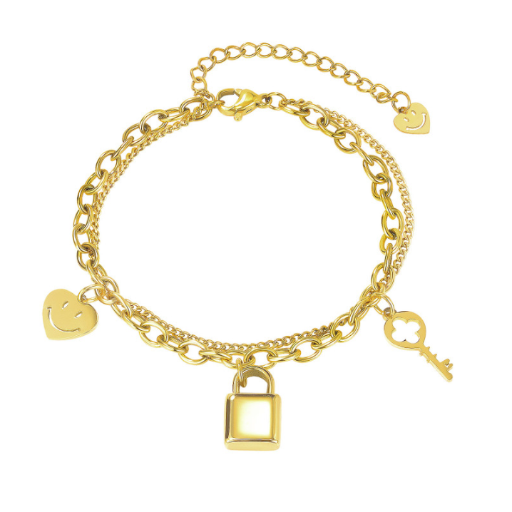 A gold-tone double-chain charm bracelet featuring a padlock, a key, and two smiley-face heart charms, displayed on a clean white background.