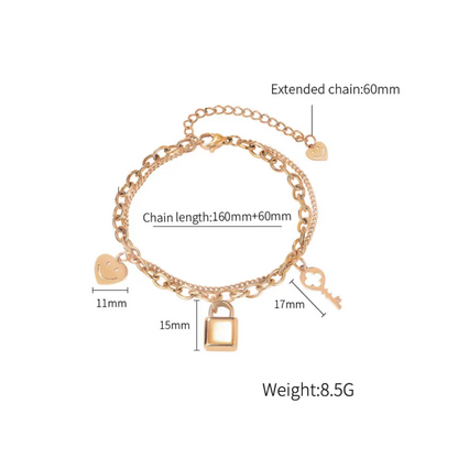 Rose gold plated chain bracelet with a padlock, key, and heart charms, shown with measurement labels and text indicating chain length, extension, and weight on a white background.
