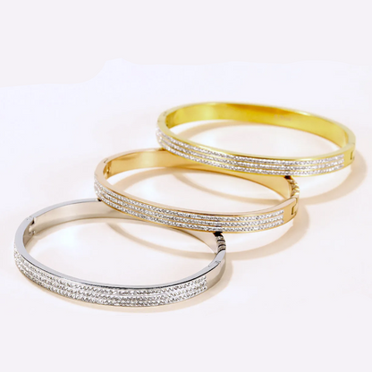 Three slim bangle bracelets arranged diagonally on a white background, featuring silver, gold, and two-tone metal bands with rows of clear pavé stones.