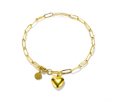 A gold paperclip chain bracelet with a polished heart charm and a small round disc charm, displayed on a clean white background.